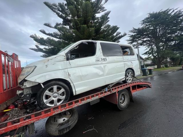 Crash-wrecked white van on a flatbed truck during free removal
